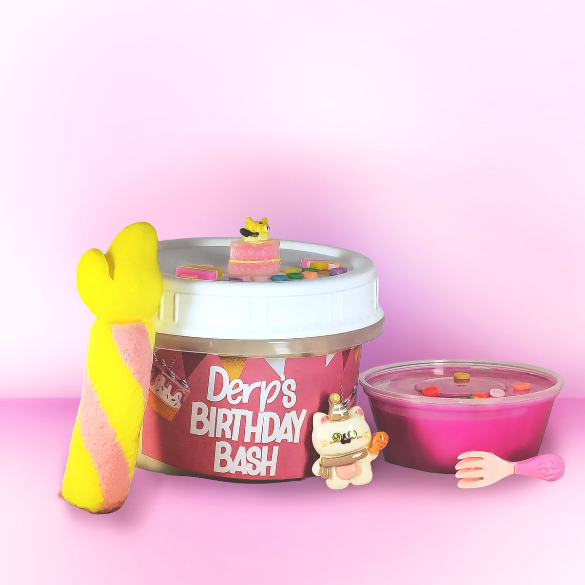 A novelty toy or container labeled 'Derp's Birthday Bash' filled with pale yellow material and decorated with bright pink icing-like drizzle, sprinkles, a yellow mermaid tail, and a small white cat figurine, set against a pink gradient background.