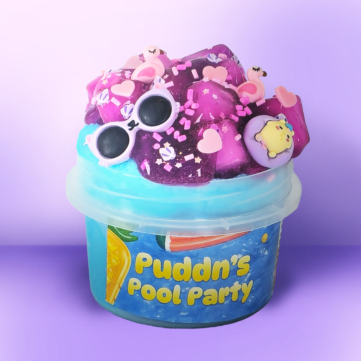 A novelty party slime bucket from Puddn's Pool Party, filled with pink and purple glitter slime topped with decorative charms including sunglasses, hearts, flamingos, and a yellow duck, set against a purple gradient background.
